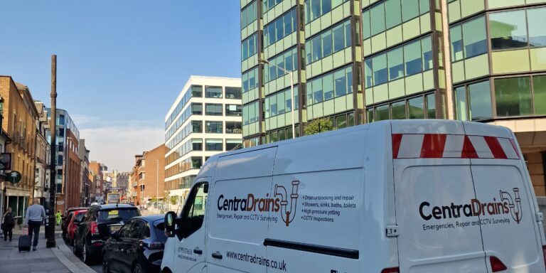 High-angle photo of a Centra Drains service van parked on an urban street with modern office buildings in the background.